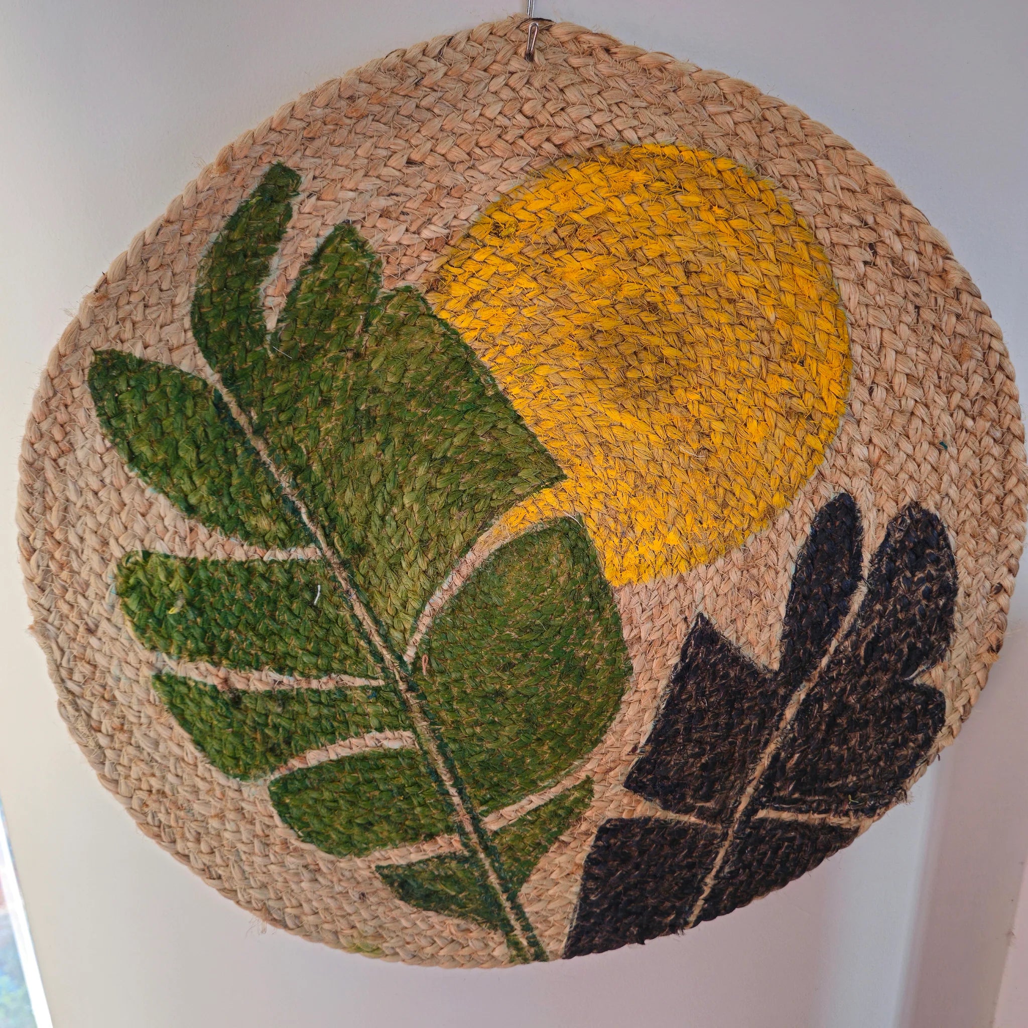Round woven mat with yellow sun and green leaves design on a plain background