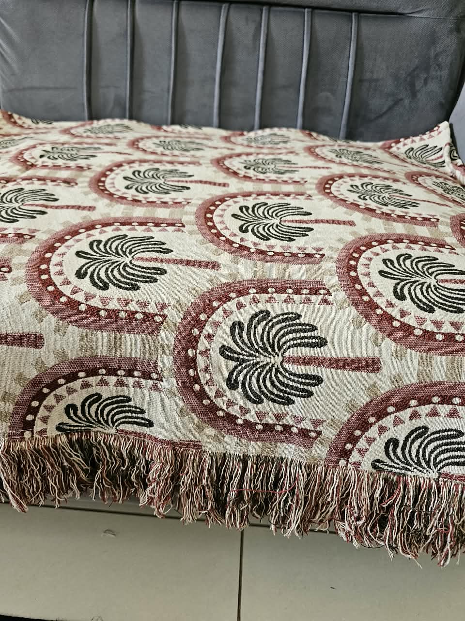 Vasaca handwoven jacquard cotton sofa cover featuring an arch and palm tree pattern with tassels on a grey sofa.