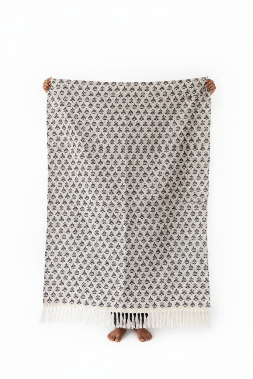 Vasaca off-white handwoven cotton runner with black botanical leaf motif pattern held up for display.