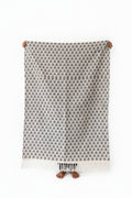 Vasaca off-white handwoven cotton runner with black botanical leaf motif pattern held up for display.