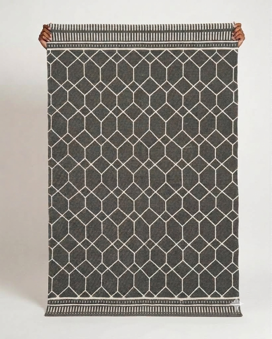 Vasaca charcoal dark grey handwoven cotton flatweave runner rug with off-white geometric lattice pattern, striped end-borders, and tassels.