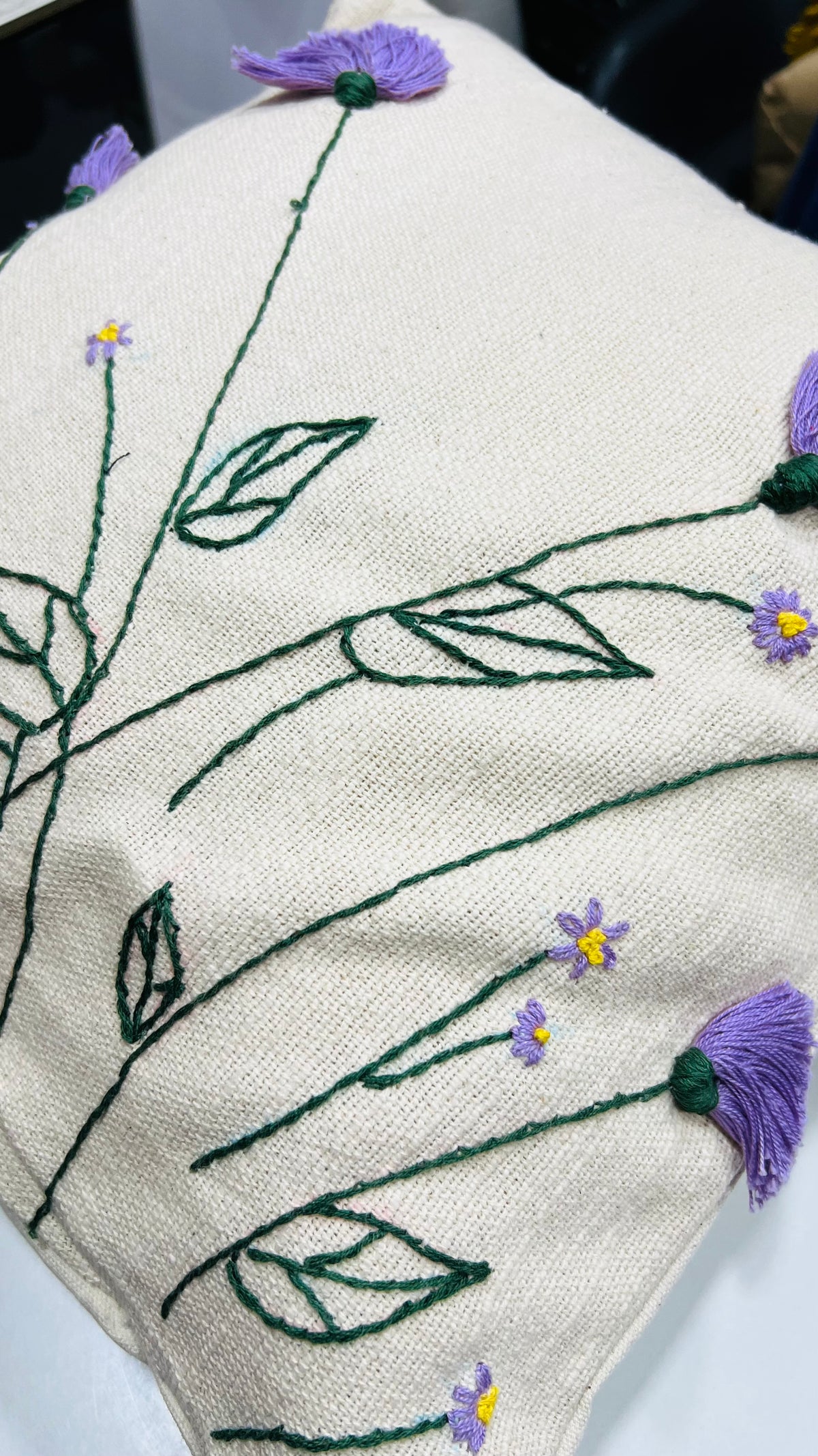 Vasaca jute-cotton handcrafted floral embroidered throw pillow cover featuring hand-stitched green stems and textured purple floral blooms on a natural off-white jute-cotton base.