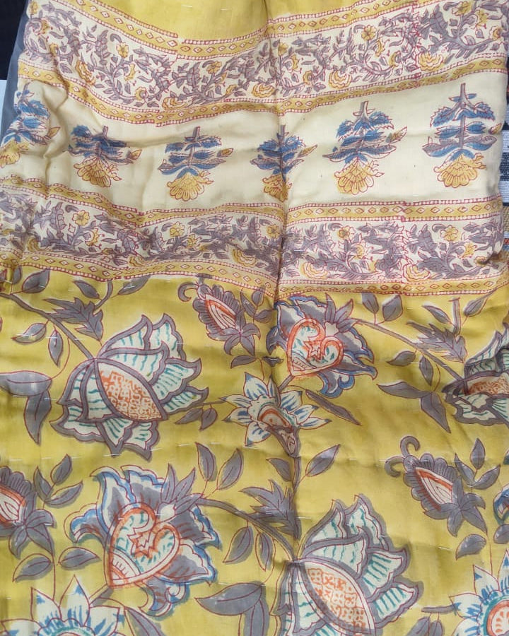 Close-up view of a Vasaca reversible handblock printed cotton single bed razai featuring a mustard yellow background with floral patterns and quilted texture.