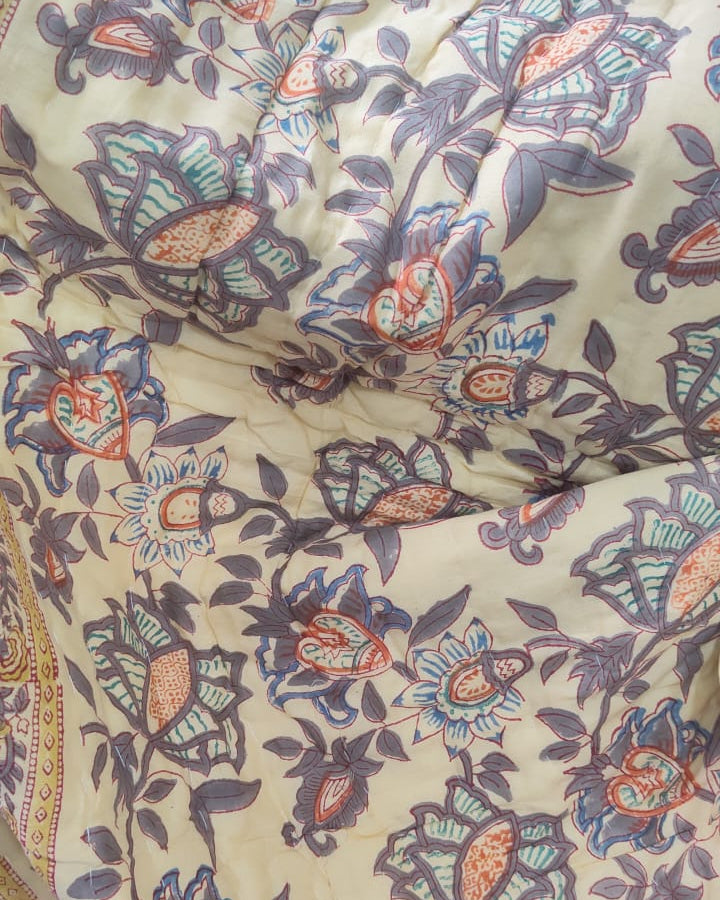Close-up view of a Vasaca reversible handblock printed cotton single bed razai featuring a mustard yellow background with floral patterns and quilted texture.
