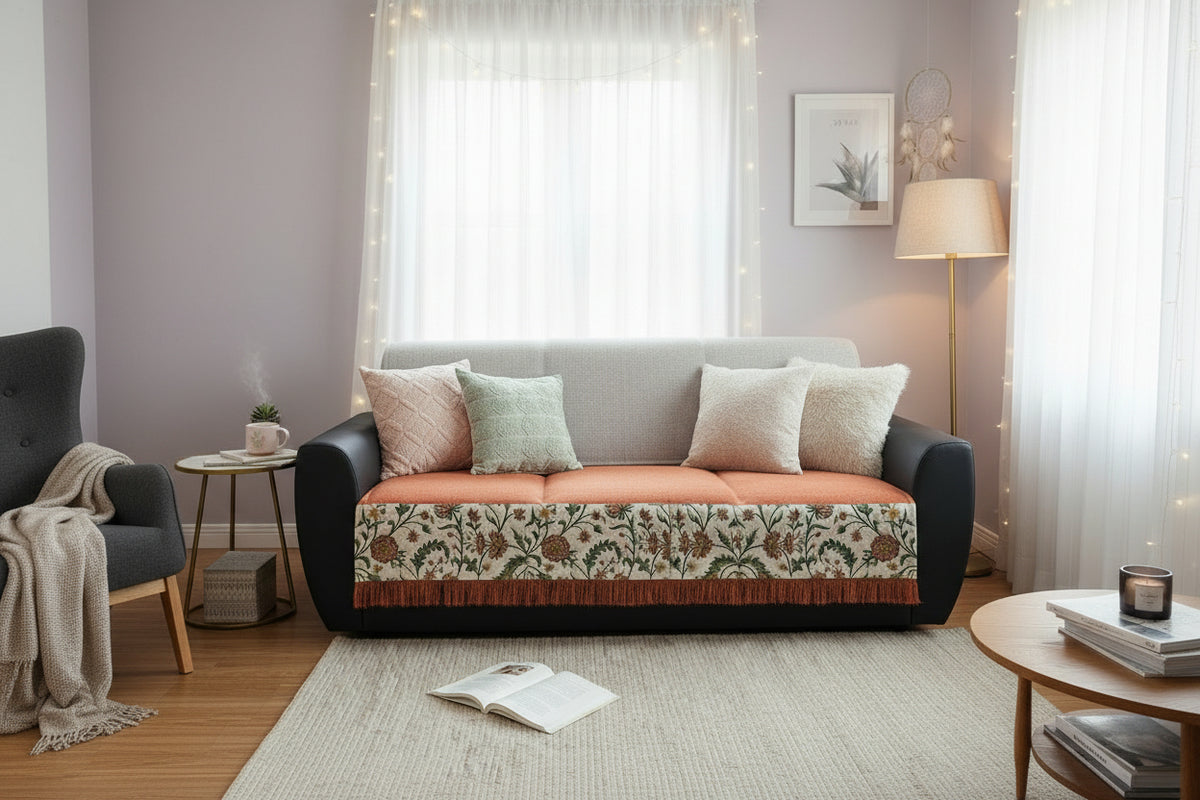 Vasaca rust-orange jute-cotton seat-only sofa runner with an off-white floral embroidered border and fringe trim, neatly covering only the seat cushions of a classic 3-seater tufted sofa in a traditional room setting.