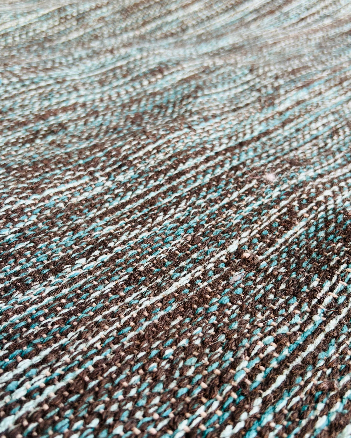 Vasaca handwoven flatweave rug displaying a heathered pattern of teal green and dark slate charcoal yarns laid flat.