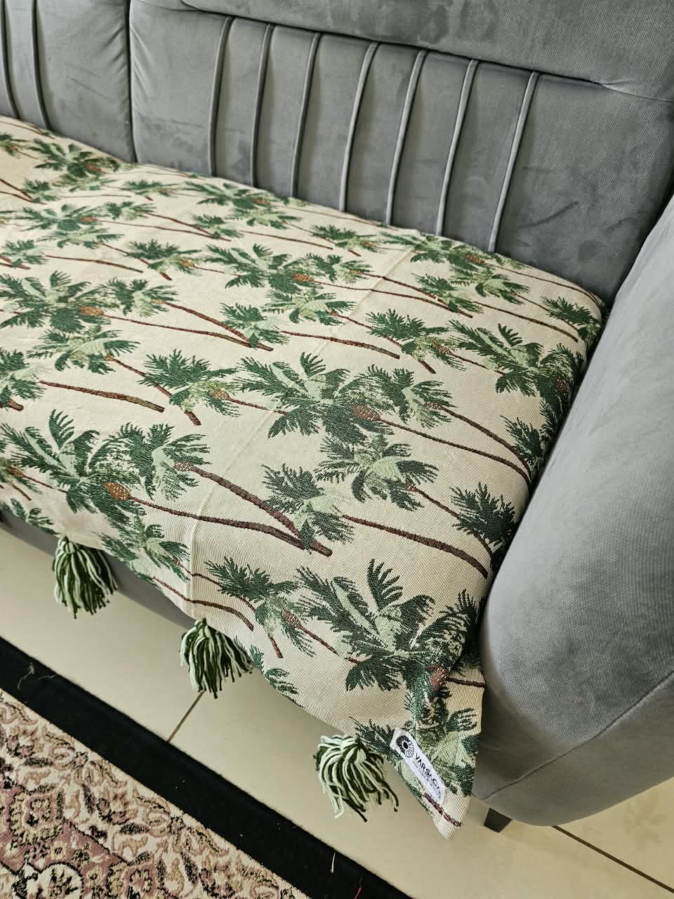 Vasaca handwoven cotton sofa runner featuring a green tropical palm tree pattern and decorative tassels on a grey sofa.