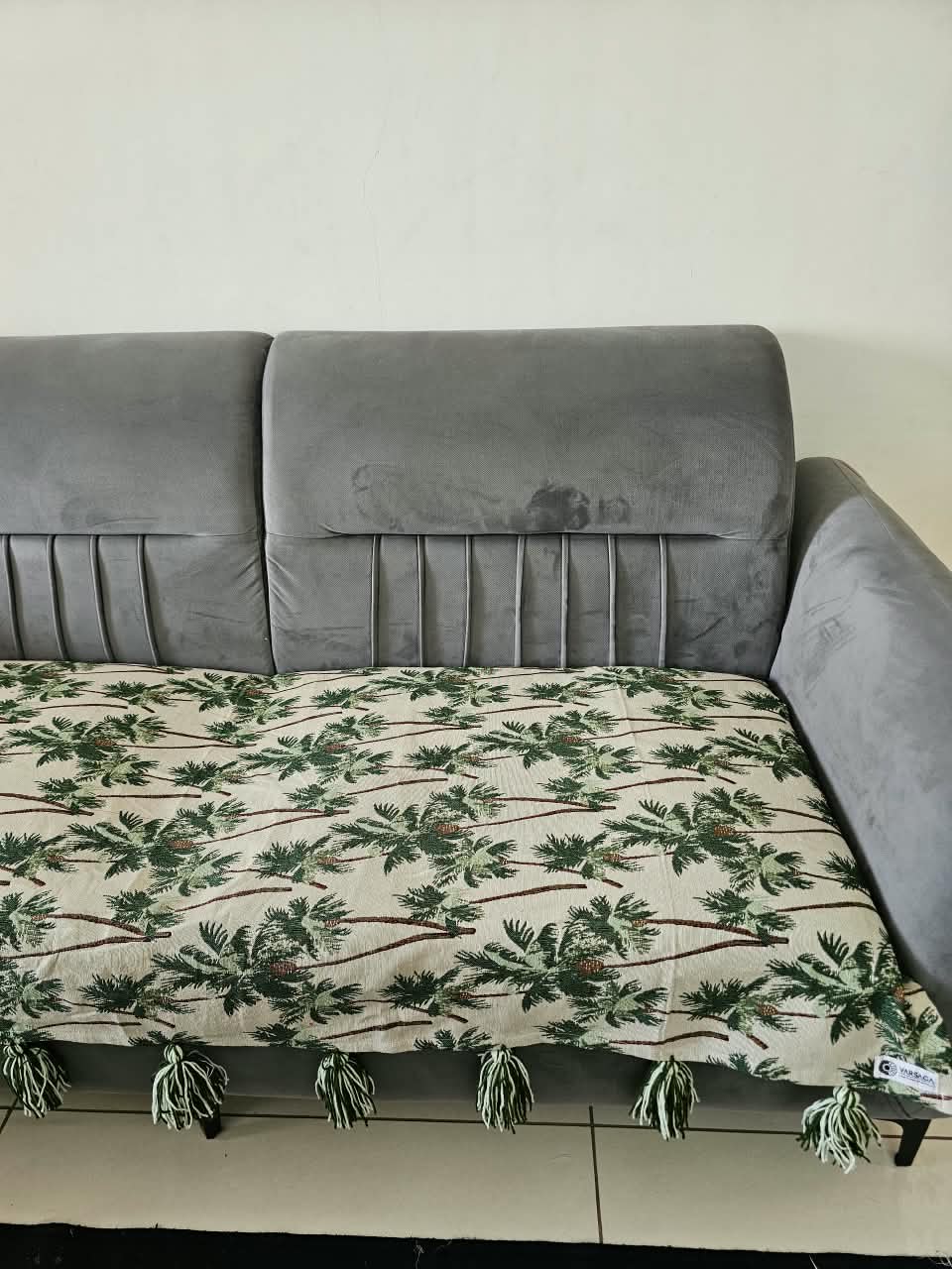 Vasaca handwoven cotton sofa runner featuring a green tropical palm tree pattern and decorative tassels on a grey sofa.