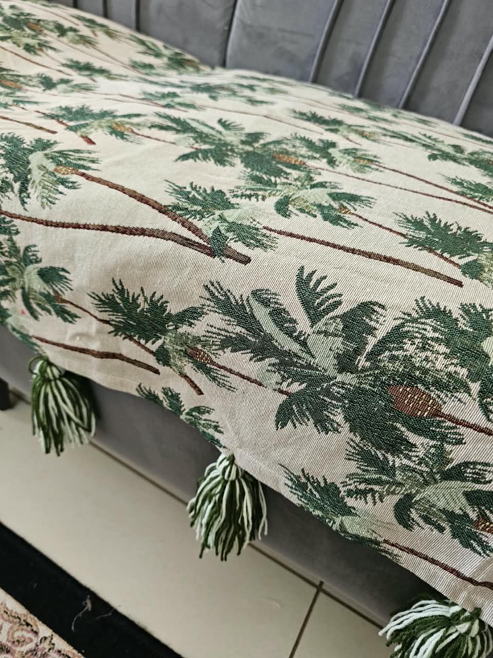 Vasaca handwoven cotton sofa runner featuring a green tropical palm tree pattern and decorative tassels on a grey sofa.