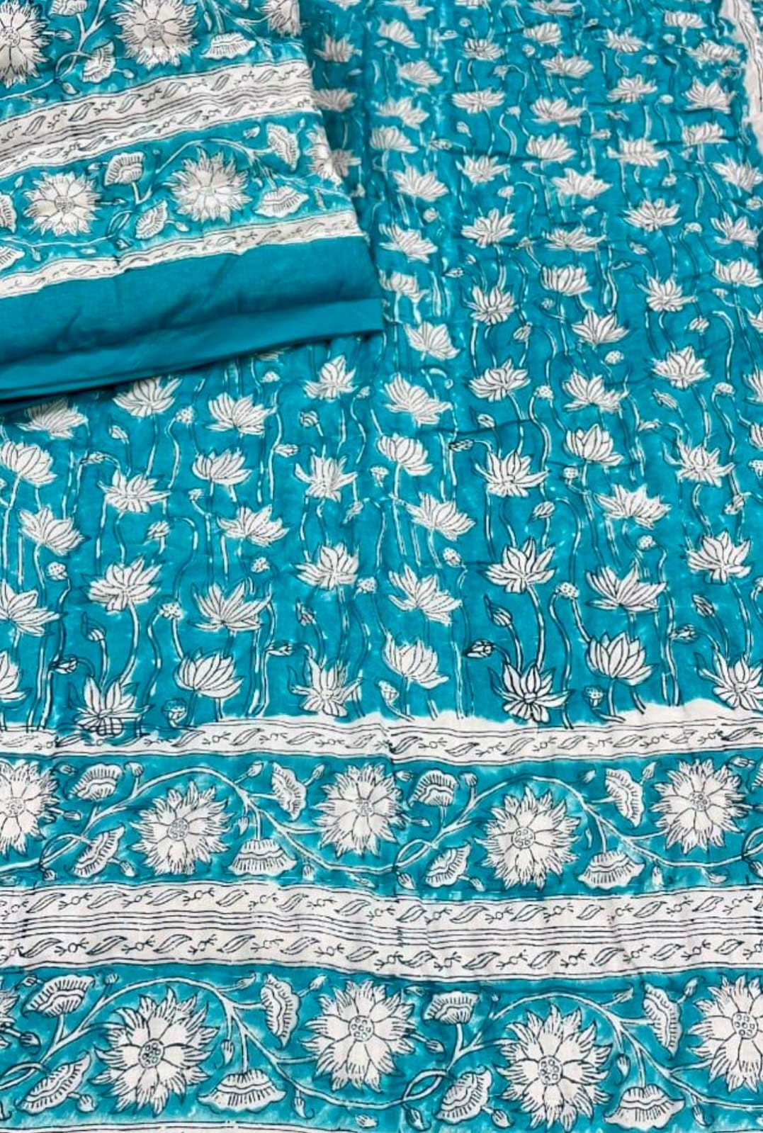 Close-up view of a Vasaca handblock printed cotton single bed razai featuring a vibrant turquoise blue background with white lotus floral patterns and bordered edges.