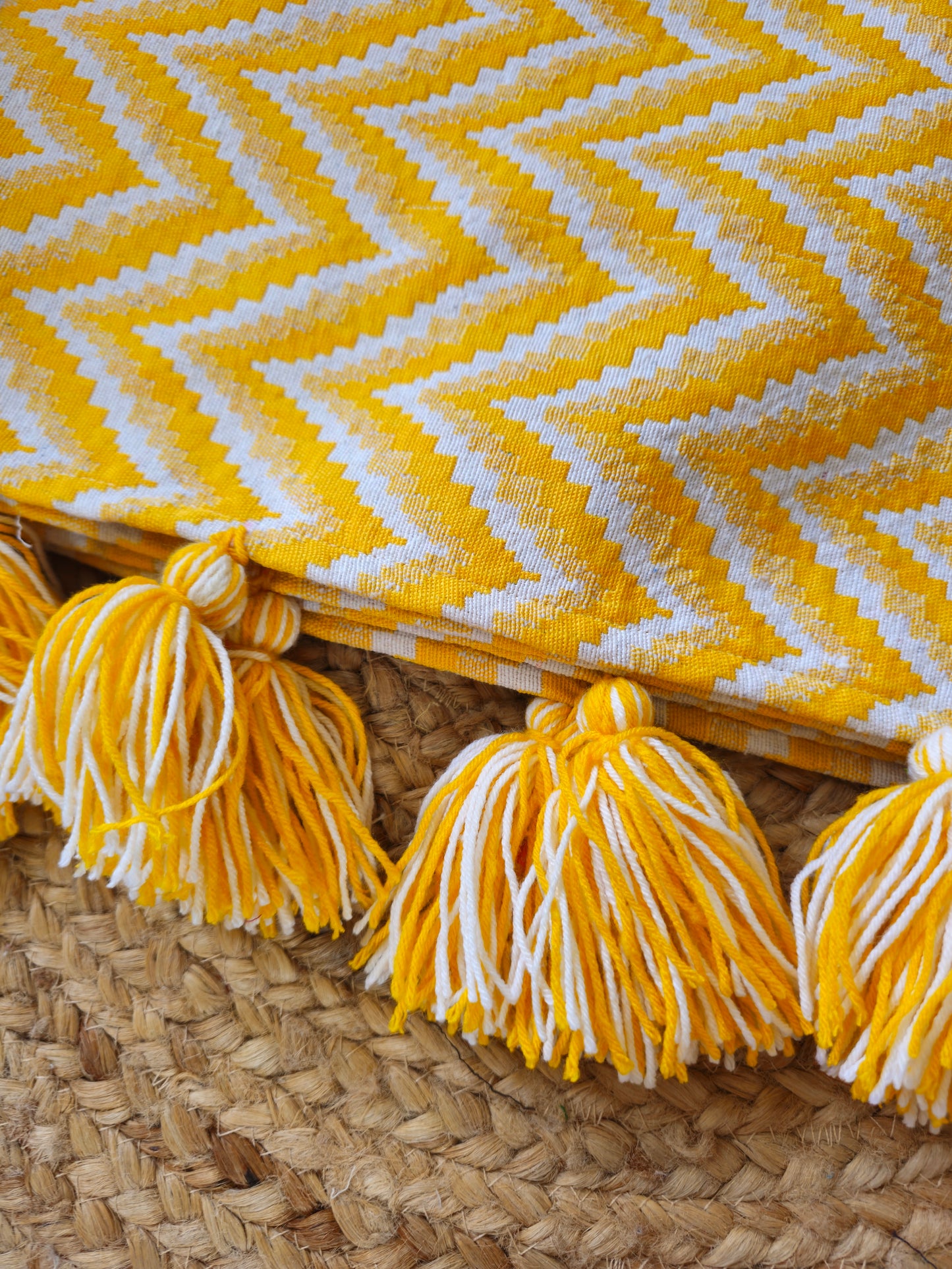 Yellow and white chevron patterned blanket with tassels on a woven surface