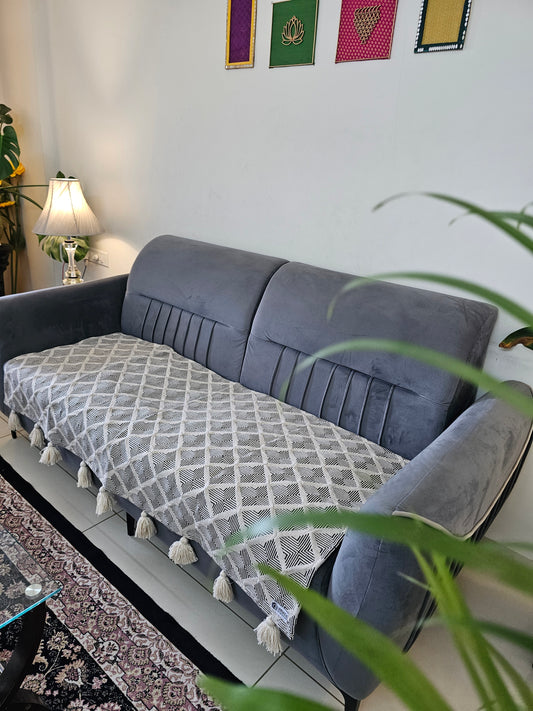 Gray sofa with a patterned cushion in a room with a white wall and decorative items.
