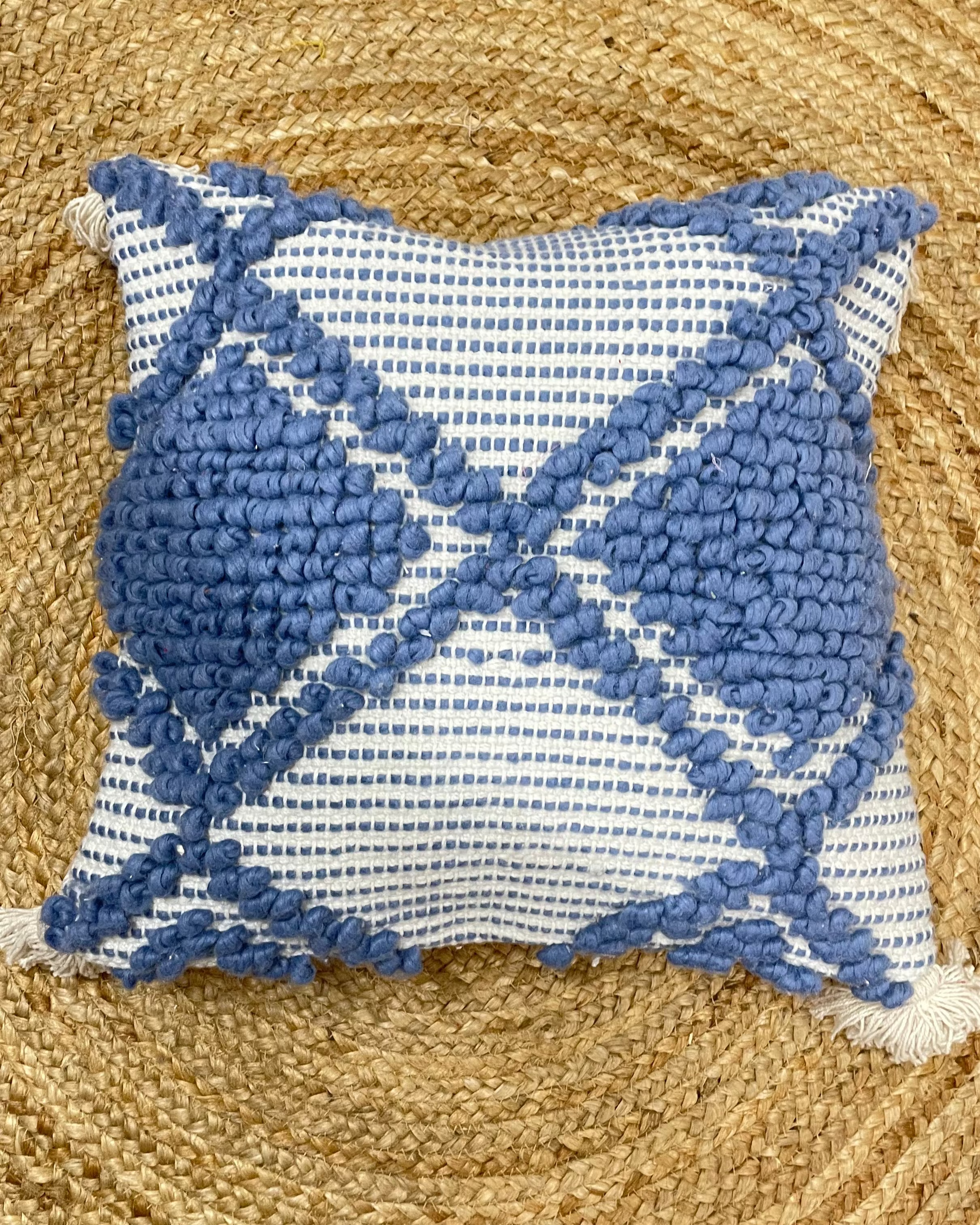 Set of 5 coastal boho-style cotton cushion covers, featuring two end pillows with blue tufted diamonds, two inner pillows with textured blue patterns, and a central white pillow with blue tufted lines and tassels, arranged neatly on a blue sofa in a bright living room.