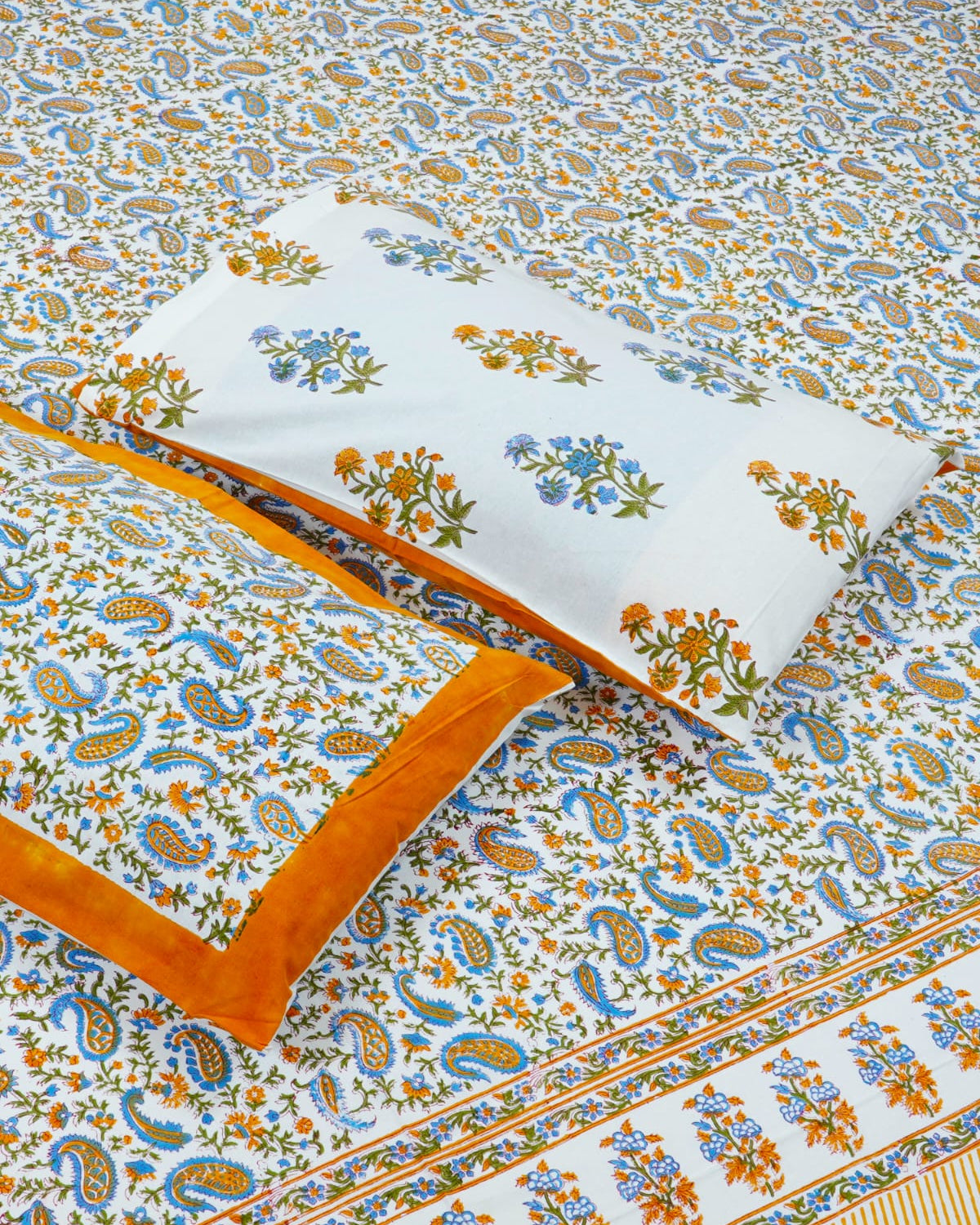 00x108 inch king size cotton bedsheet and matching solid orange-bordered pillow covers styled with a traditional blue and orange paisley handblock print.