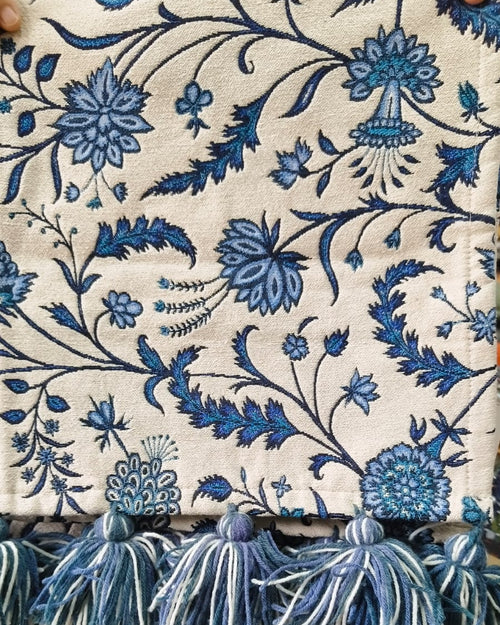 Blue and white floral Jacquard cotton dining table runner featuring an intricate botanical vine pattern and two-tone woolen hanging tassels, with Vasaca brand labels.