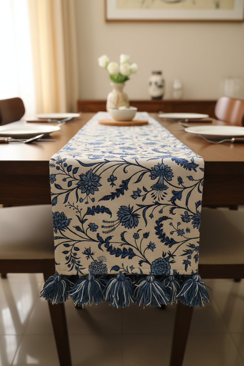 Blue and white floral Jacquard cotton dining table runner featuring an intricate botanical vine pattern and two-tone woolen hanging tassels, with Vasaca brand labels.
