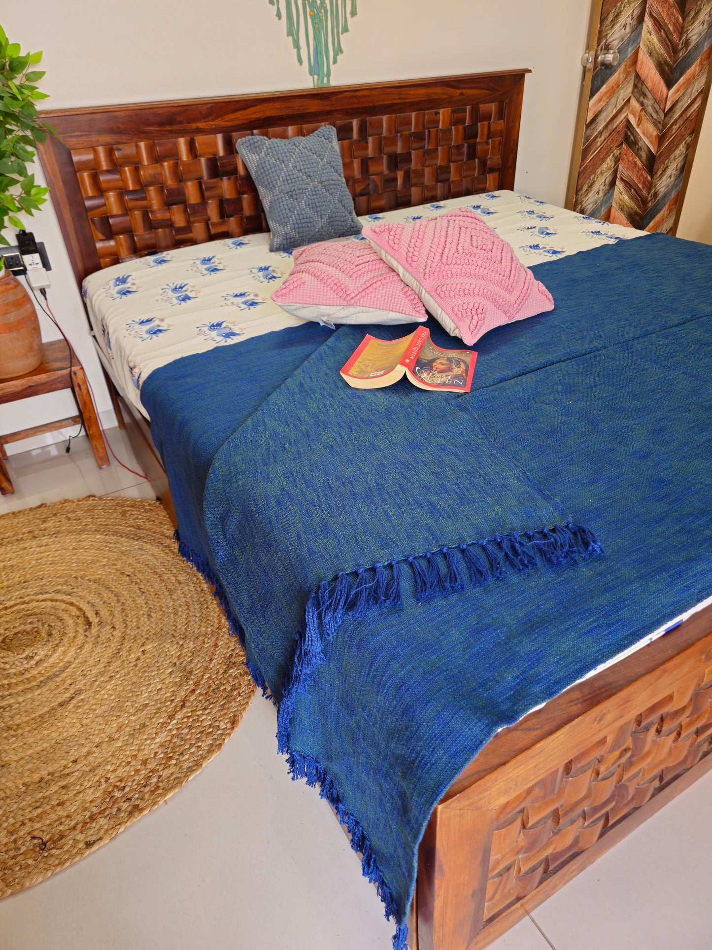 Bed with wooden headboard, blue throw blanket, and pink pillow in a room setting.