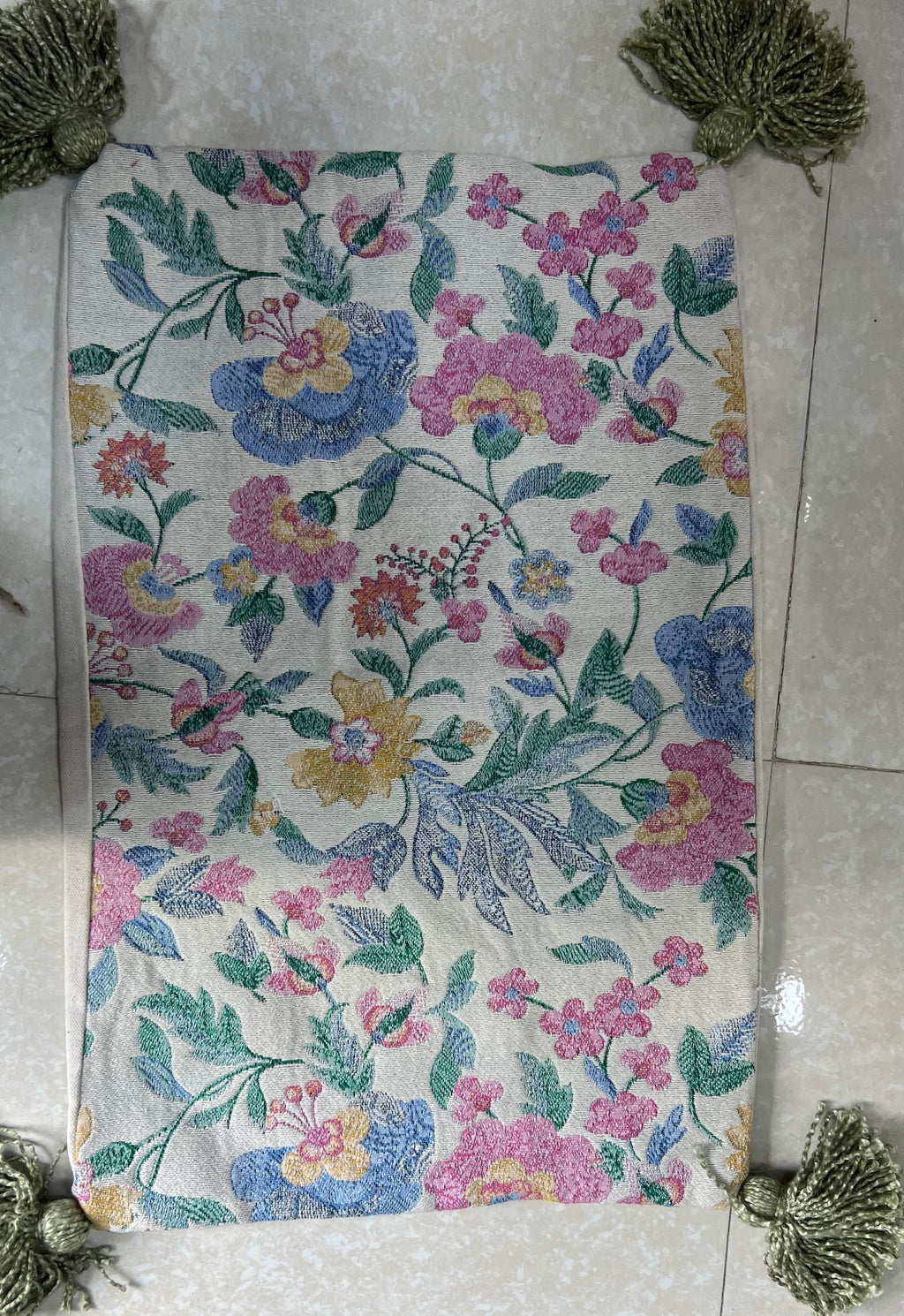 Rectangular boho-style cotton cushion cover featuring a vintage botanical floral pattern in pink, blue, and yellow, complete with sage-green corner tassels, laid flat on a light surface.