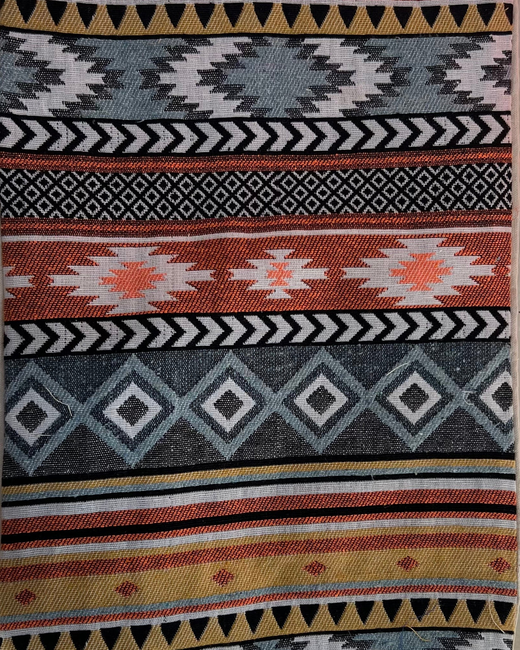 Rectangular boho-style cotton cushion cover featuring a colorful tribal geometric pattern in yellow, grey, and orange, complete with mustard corner tassels and grey center tassels, laid flat on a light surface.