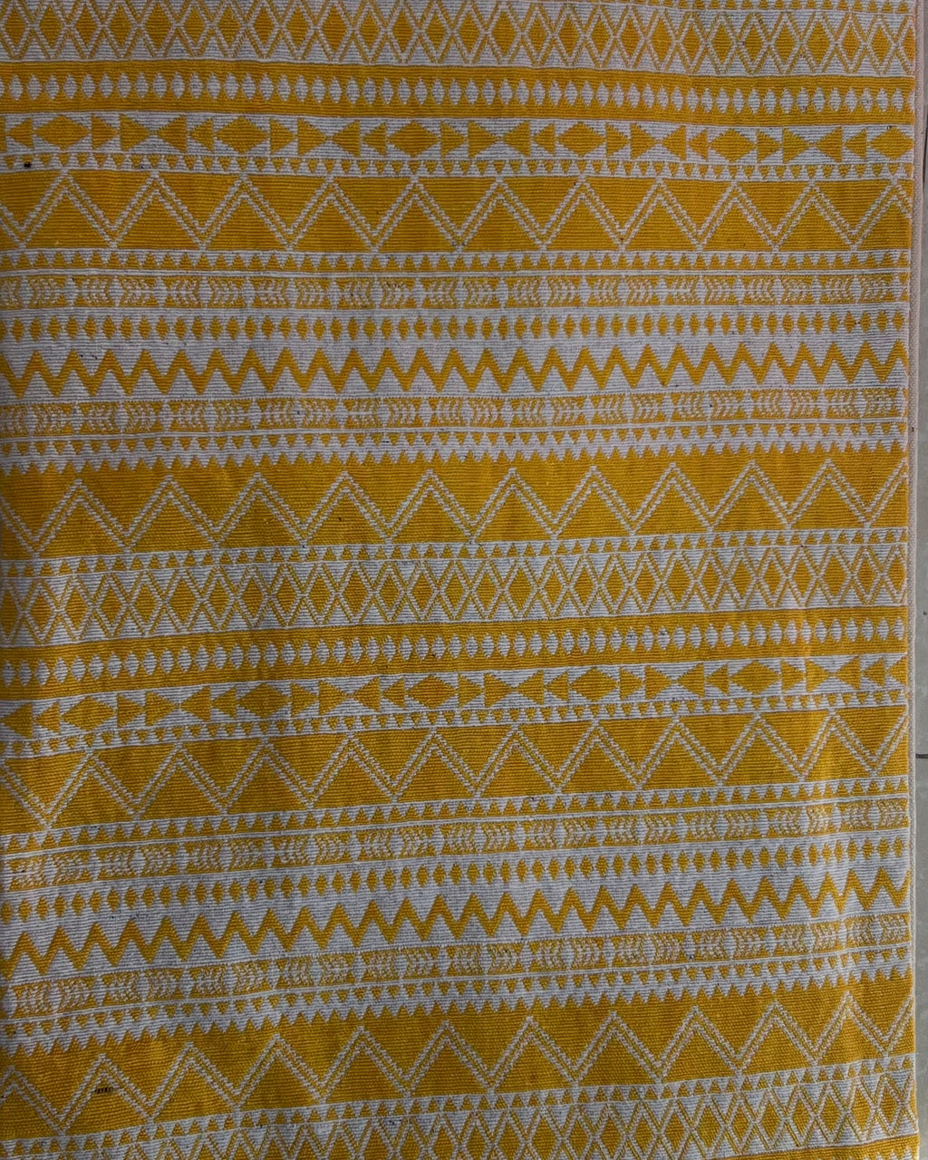 Rectangular boho-style cotton cushion cover featuring a geometric zigzag pattern in mustard yellow and white, complete with yellow-and-white corner tassels and white center tassels, laid flat on a light surface.