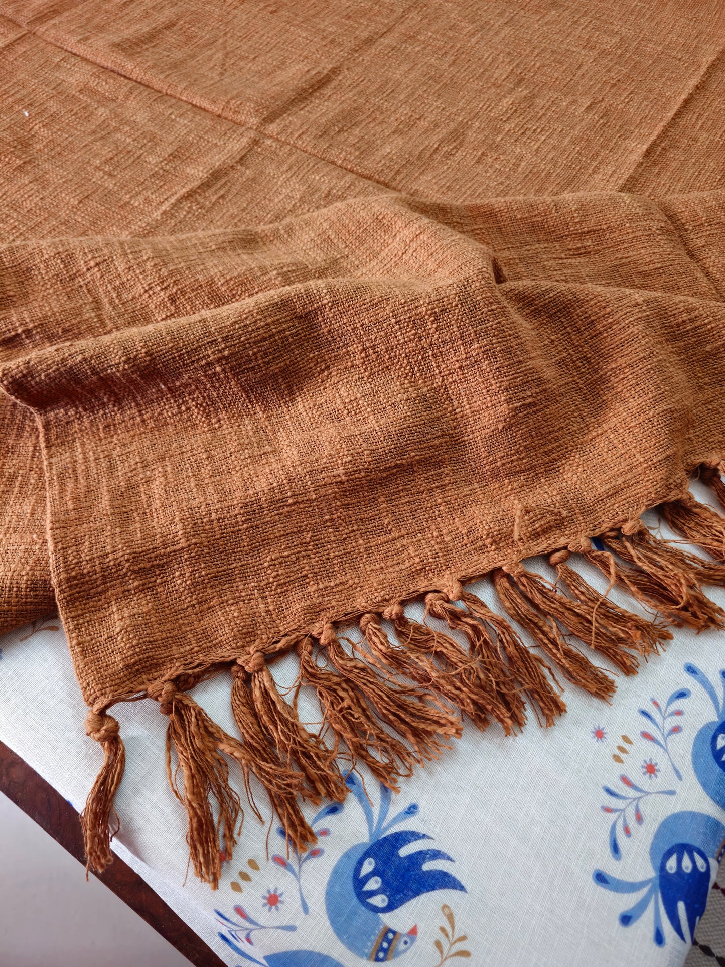 Brown woven blanket with fringes on a white surface with blue patterns