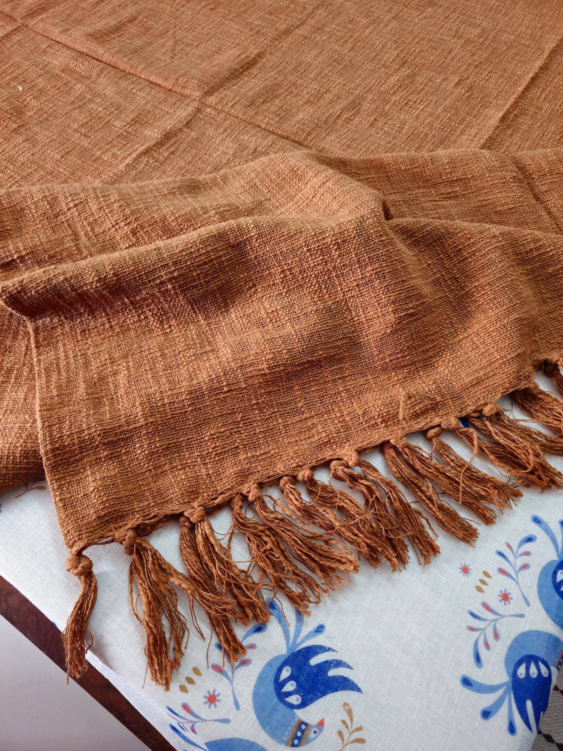 Brown woven blanket with fringes on a white surface with blue patterns