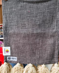 Charcoal grey jute-cotton handloom table runner featuring chunky off-white woolen hanging tassels and Vasaca brand labels.
