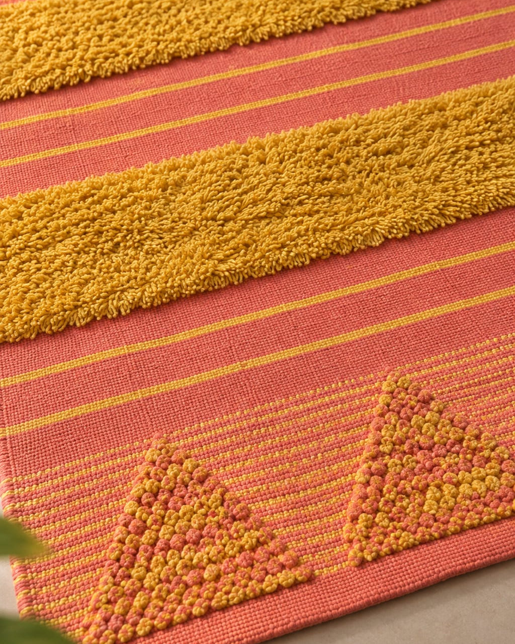 Coral and mustard handwoven cotton tufted rug featuring raised geometric triangle motifs and plush textured stripes in a modern living room setup.