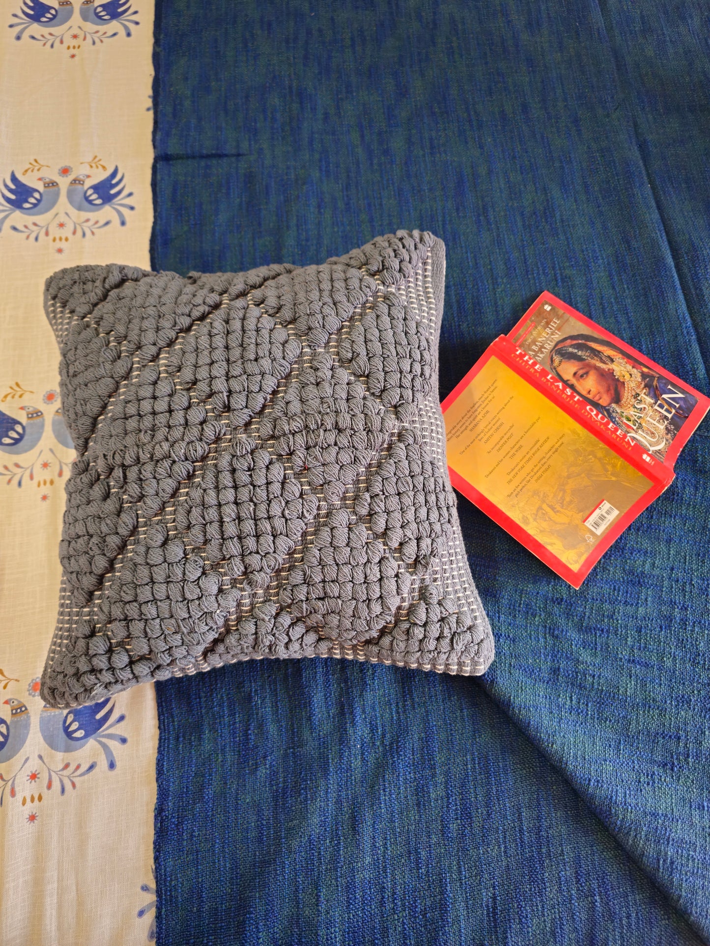 Gray textured pillow on a blue fabric surface with a colorful card beside it.