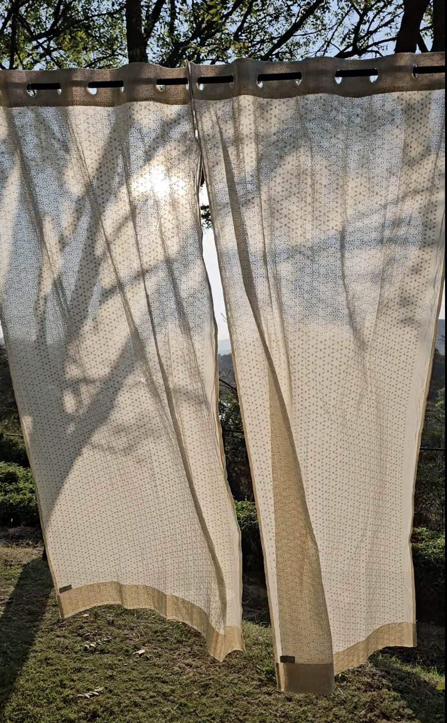 Beige outdoor curtains with a subtle pattern hanging outdoors.