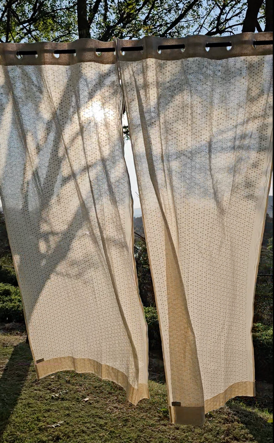 Beige outdoor curtains with a subtle pattern hanging outdoors.