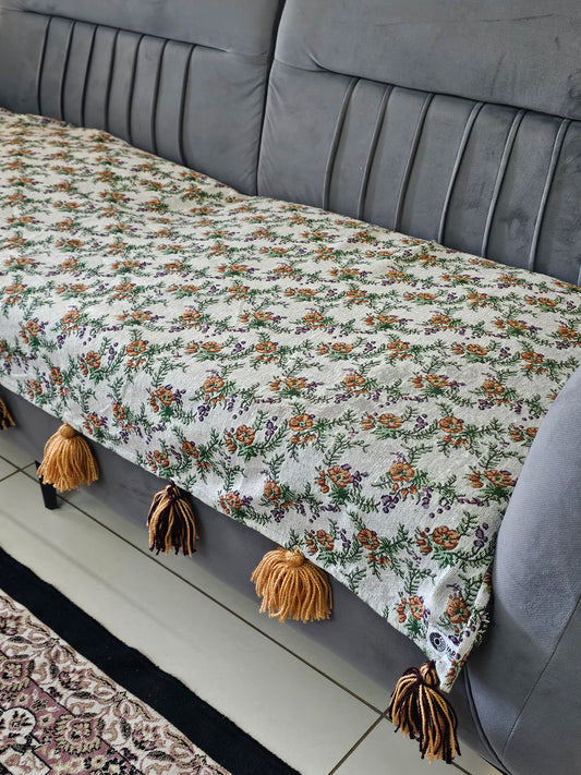 Floral-patterned blanket with tassels draped over a gray sofa.