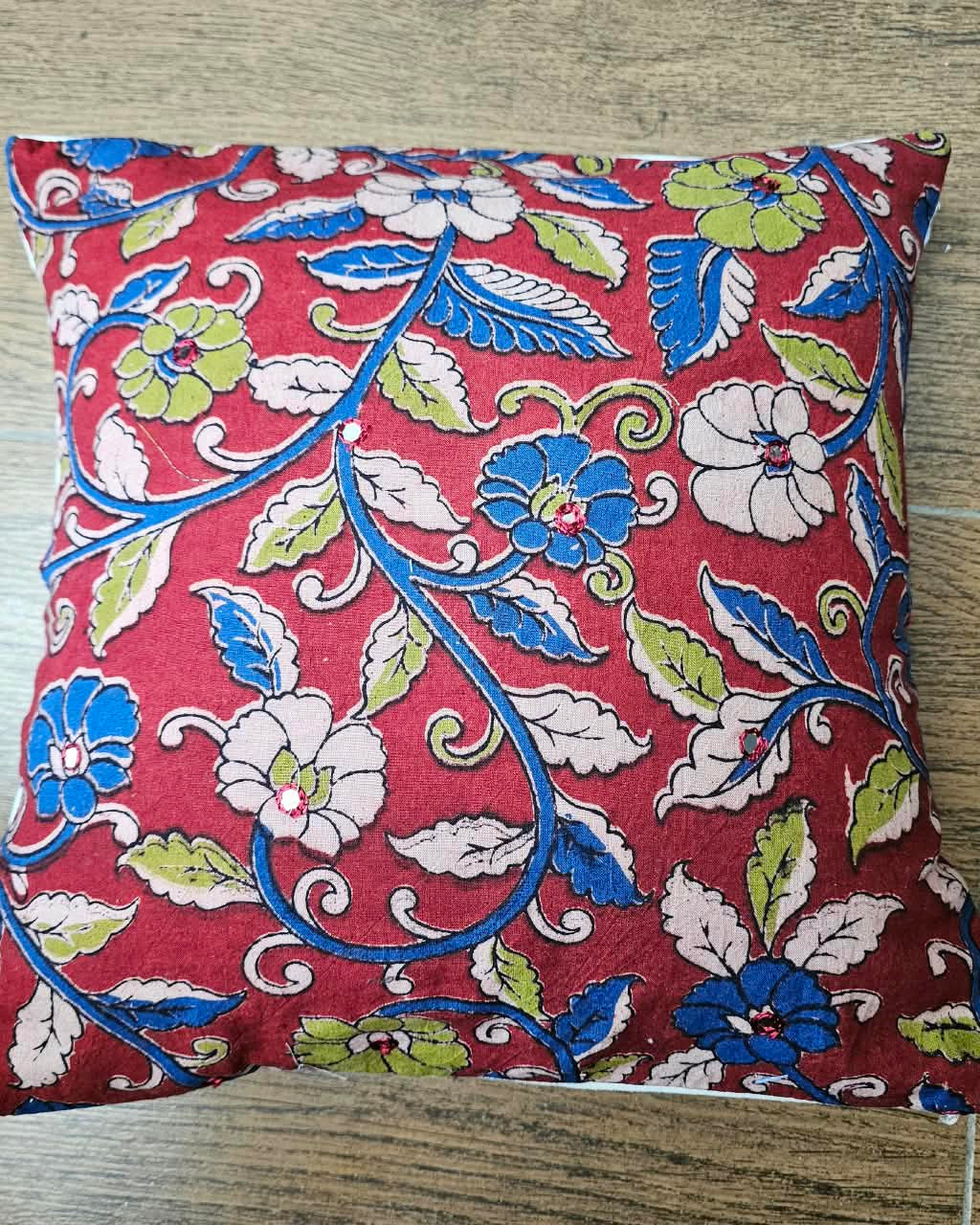 Crimson red cotton cushion cover featuring traditional blue and floral handblock vine prints with subtle accent embellishments.