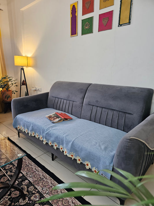 Gray sofa with floral trim in a room with colorful wall art and a plant.