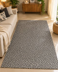 Off-white cotton area rug with an all-over charcoal black polka dot pattern styled in a warm, modern living room setup.