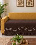 Dark chocolate brown cotton sofa cover with off-white embroidered wavy accent lines and fringed hem styled across a mustard yellow sofa seating area.