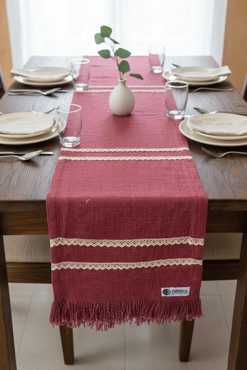 Dark pink jute-cotton handloom table runner featuring two parallel rows of off-white crochet lace trim and a matching self-fringed hem, with Vasaca brand labels.