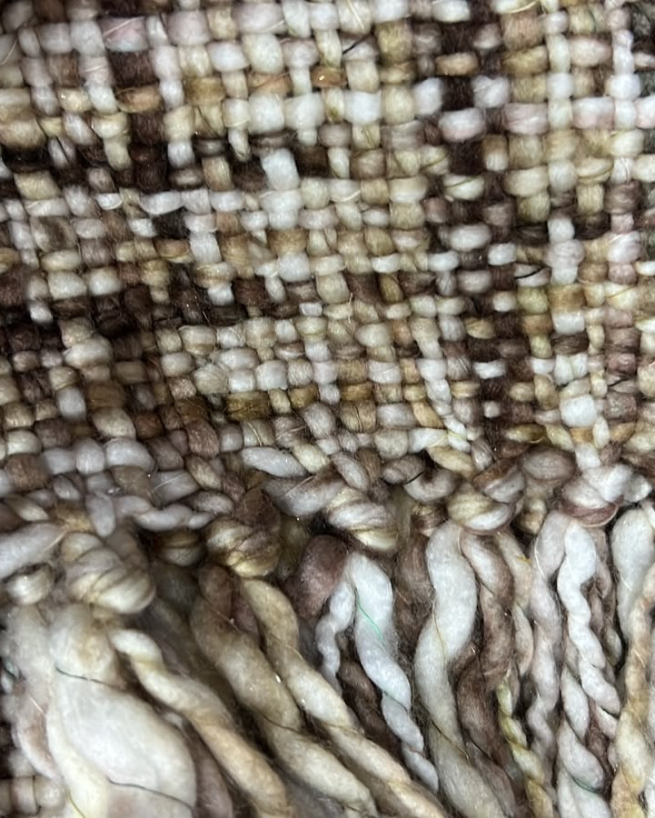 Close-up shot of an earthy chestnut brown and cream handwoven chunky woolen sofa throw featuring a textured tweed weave and thick twisted fringe tassels.