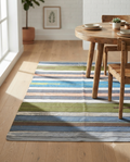 Handcrafted flatweave cotton area rug featuring horizontal multi-color stripes in earthy green, blue, peach, and brown tones.