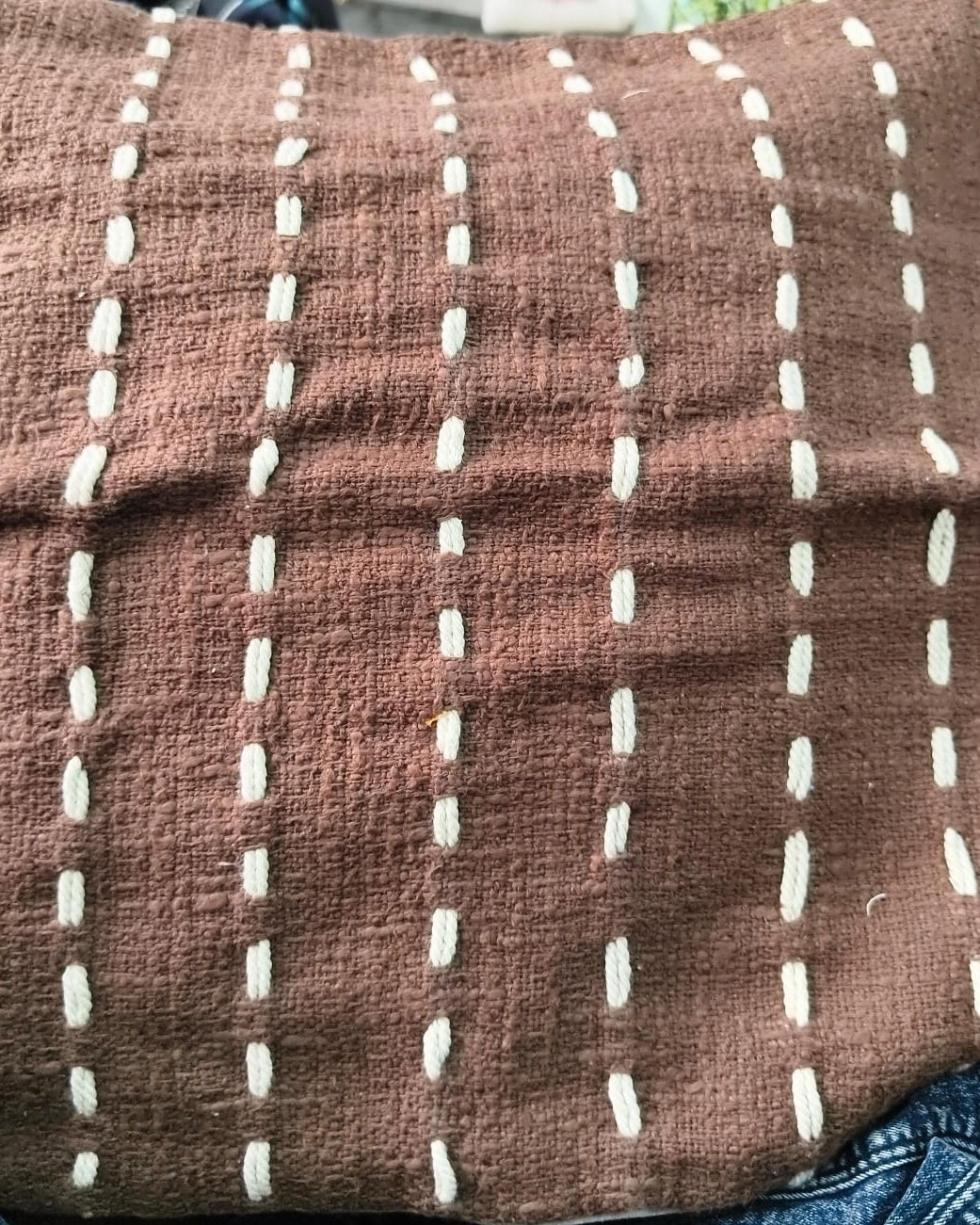 Square warm brown cotton cushion cover featuring vertical rows of cream hand-embroidered kantha running stitches.