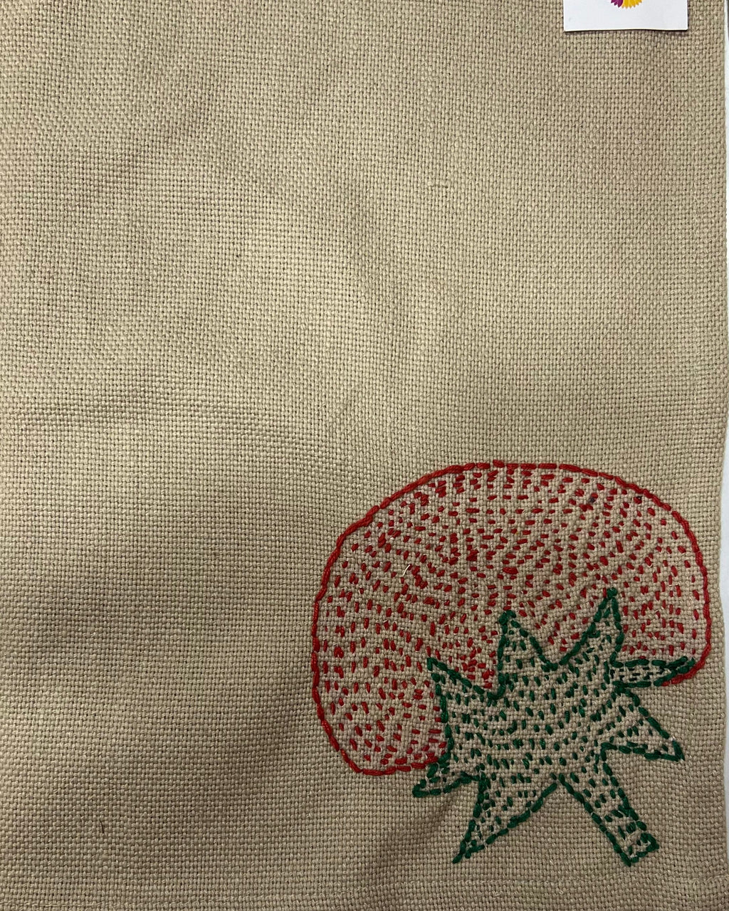 Hand-embroidered tomato motif on a natural textured burlap-style cotton placemat.