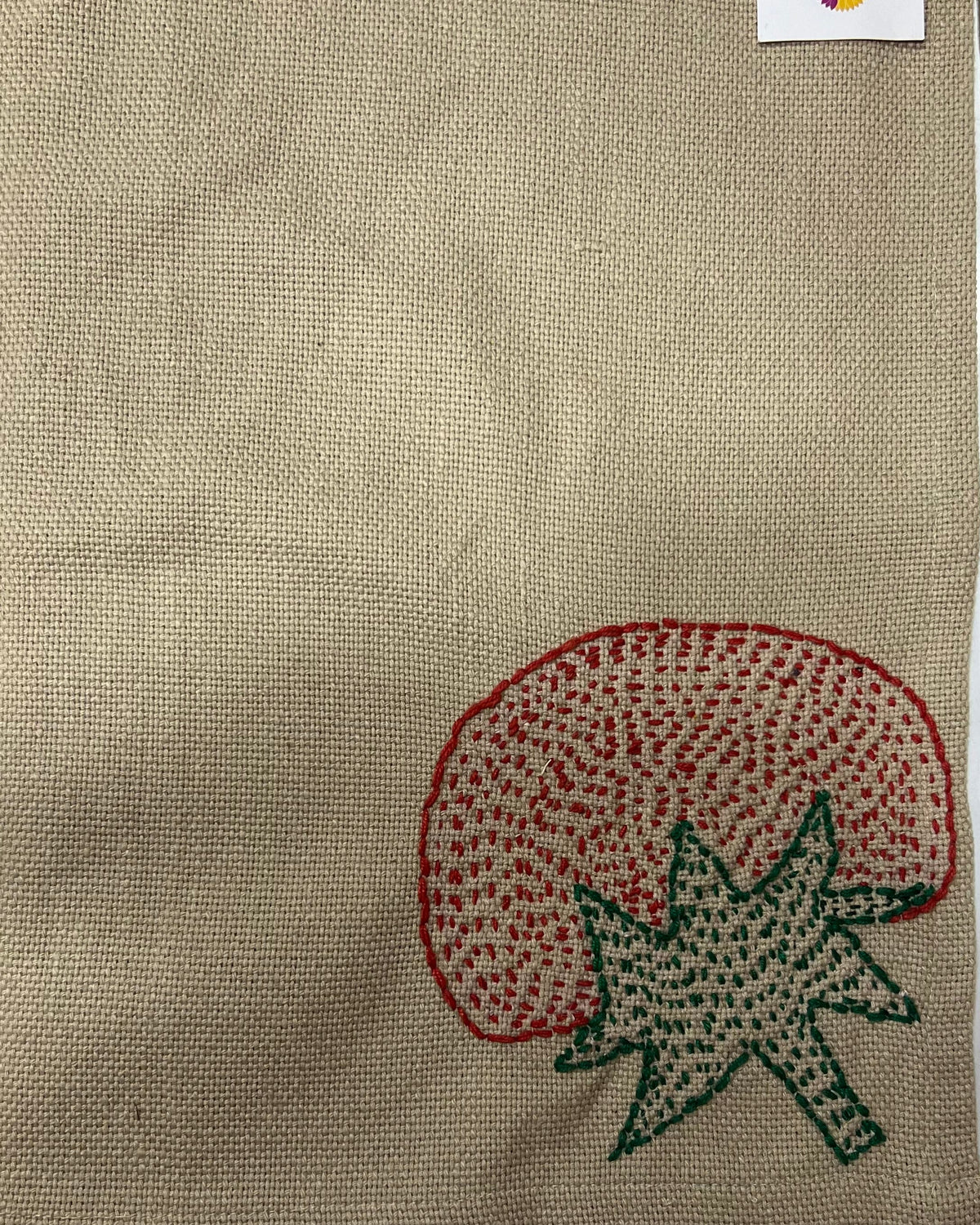 Hand-embroidered tomato motif on a natural textured burlap-style cotton placemat.