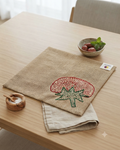 Hand-embroidered tomato motif on a natural textured burlap-style cotton placemat.