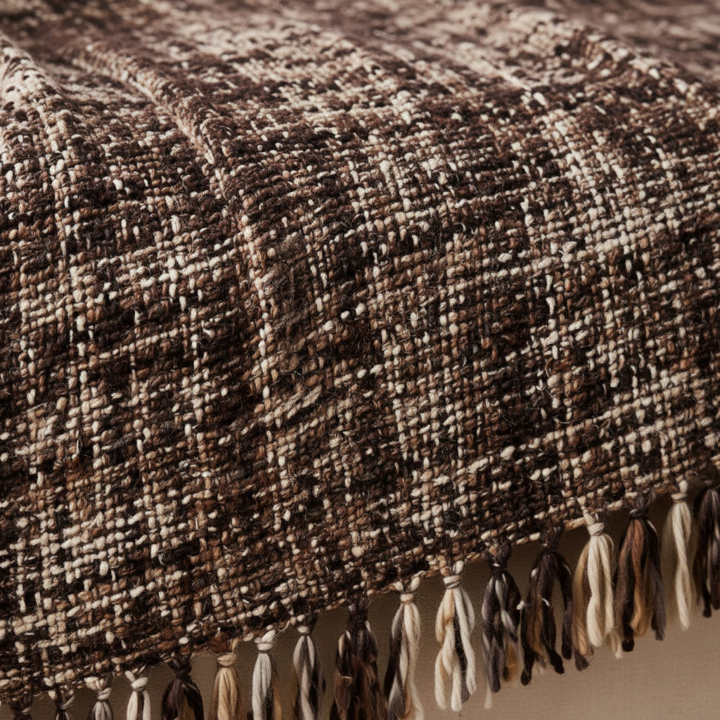 Espresso brown and cream handwoven chunky woolen sofa throw blanket featuring a textured tweed basketweave and twisted fringe draped over a beige sofa.