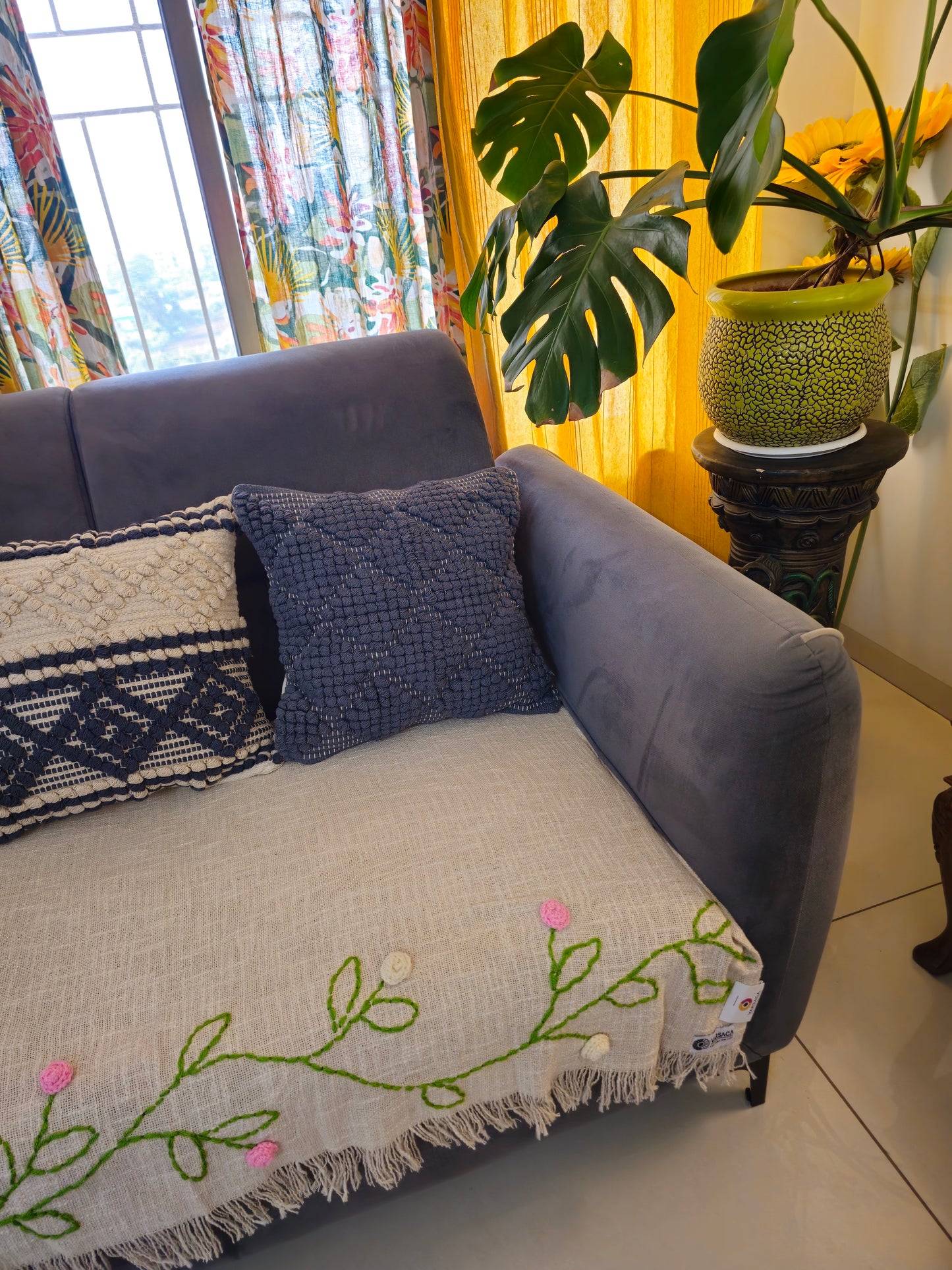 Gray sofa with decorative pillows and a floral blanket in a living room setting.