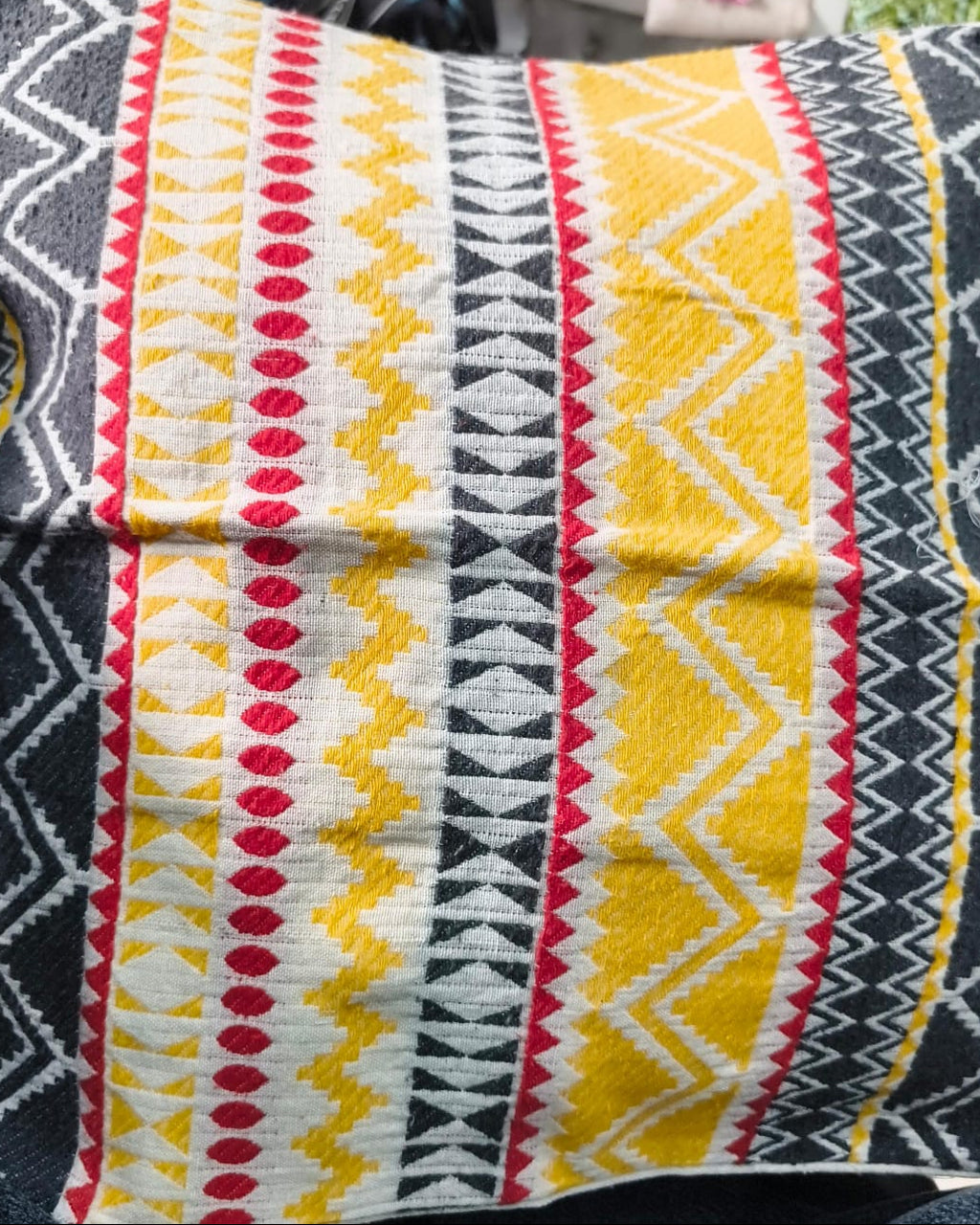 Square cream cotton cushion cover featuring a woven geometric jacquard pattern with yellow, red, and charcoal grey stripes and chevrons.