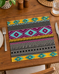 Vibrant boho-style woven table placemat featuring colorful geometric Aztec patterns in turquoise, magenta, yellow, and black, laid flat on a surface.