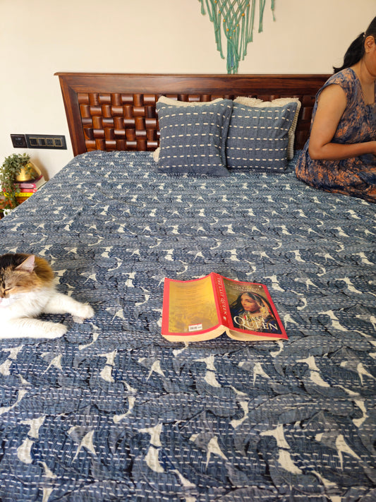 Person sitting on a bed with a cat and a book, wearing a floral dress.