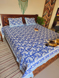 Bed with blue and white patterned quilt in a room with wooden wall art and a rug.