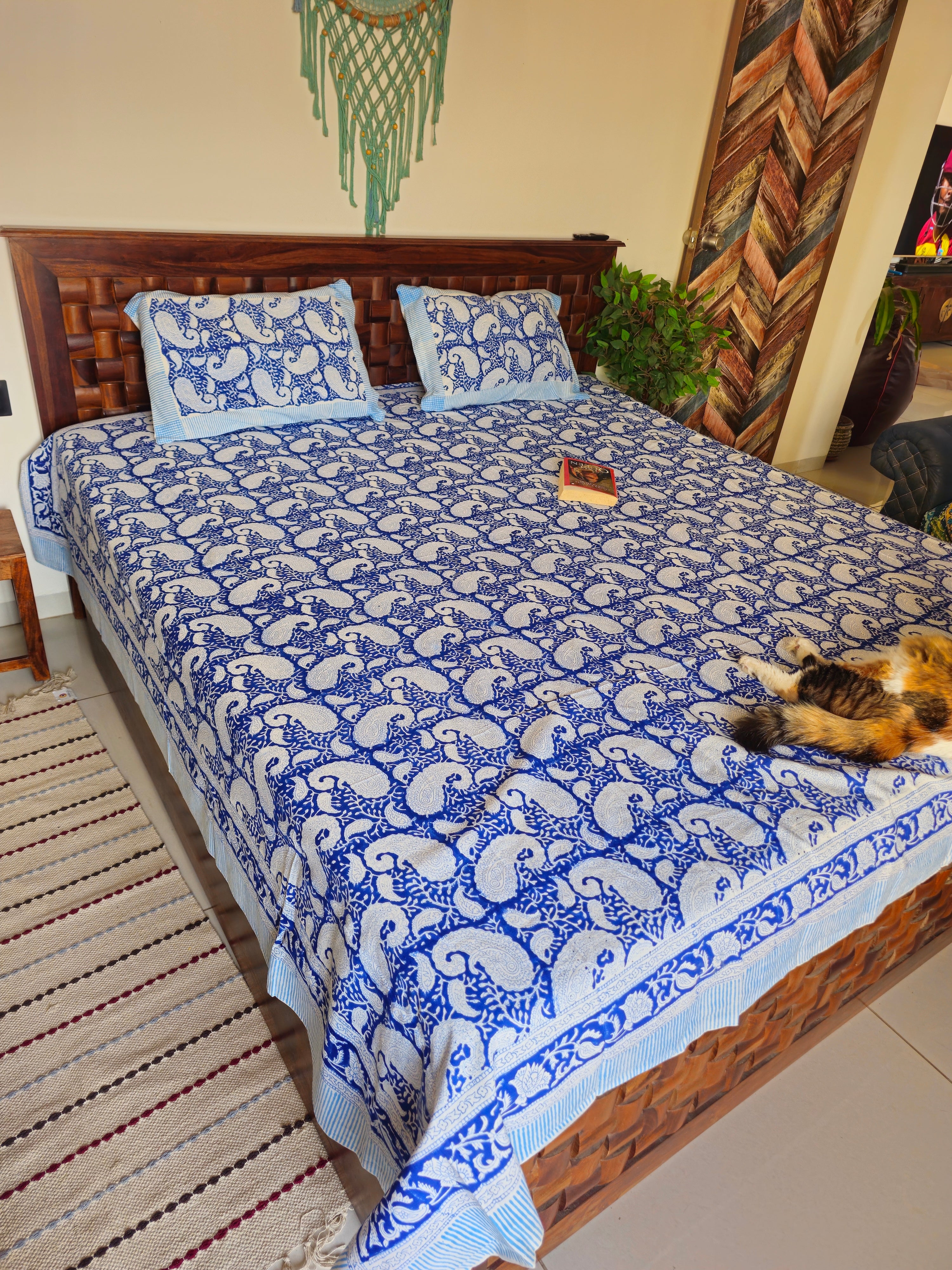 Bed with blue and white patterned quilt in a room with wooden wall art and a rug.